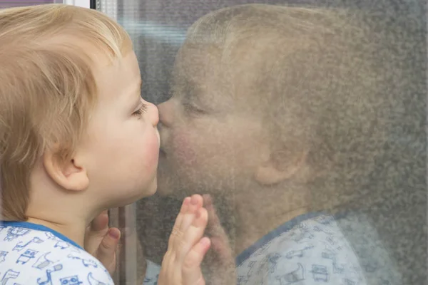 Schattig peuter leunend naar het venster en kussen zijn reflectie in de spiegel — Stockfoto