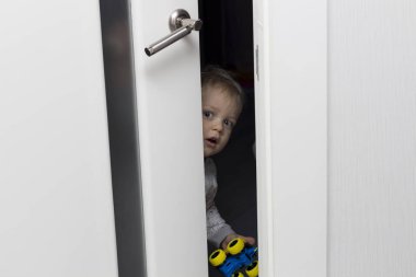 Cute toddler looking out from behind the ajar door clipart