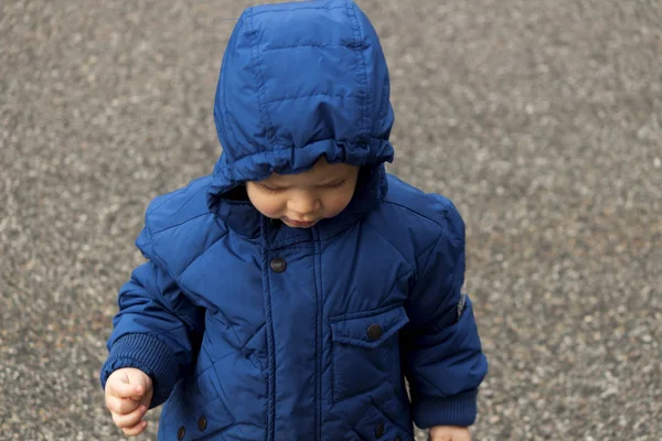 Liten pojke i en blå jacka med huva på lekplatsen — Stockfoto
