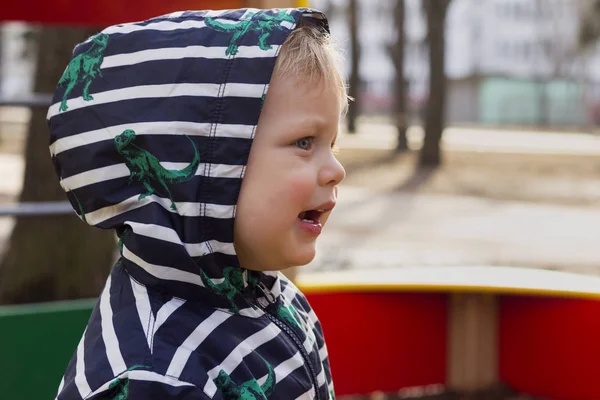 Крупный план Портрет улыбающегося мальчика, играющего на детской площадке, милого малыша в капюшоне, играющего на открытом воздухе. Копирование пространства . — стоковое фото