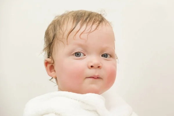 Retrato de um menino branco de olhos azuis bonito em uma toalha branca depois de um banho em um fundo branco — Fotografia de Stock