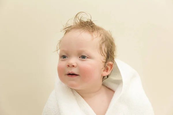 Retrato de um menino branco de olhos azuis bonito em uma toalha branca depois de um banho em um fundo branco — Fotografia de Stock