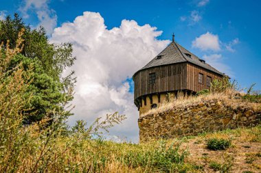 Hartenstejn, Czech Republic - August 11 2018: View of a stone tower as a part of a ruined castle built in 15th century on a green hill. Sunny summer day with bright blue sky and white clouds. 