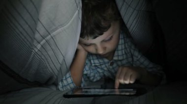 Odadaki yatakta tablet kullanan küçük çocuk. 