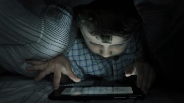 Odadaki yatakta tablet kullanan küçük çocuk. 