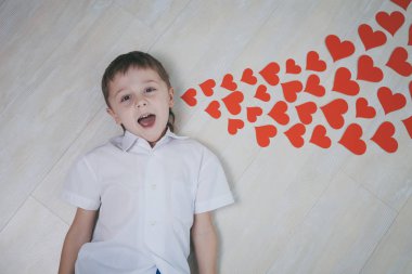 Yerde yatan küçük bir çocuk. Yalancı kağıt kalpler, ilham verici bir mesajdır. Mutlu Sevgililer Günü kavramı.