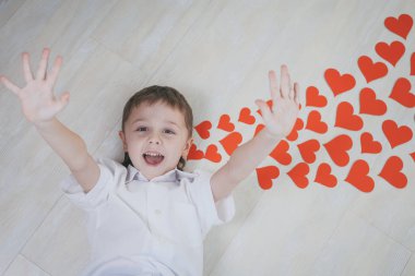 Yerde yatan küçük bir çocuk. Yalancı kağıt kalpler, ilham verici bir mesajdır. Mutlu Sevgililer Günü kavramı.
