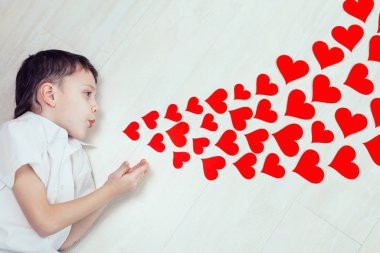 Yerde yatan küçük bir çocuk. Kağıt kalbe üflüyor, bu en sevdiği ilham verici mesaj. Mutlu Sevgililer Günü kavramı.