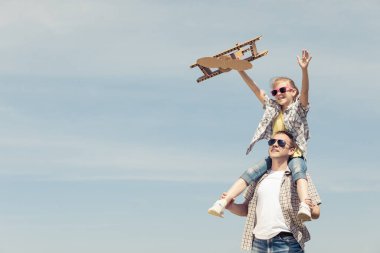 Baba ve kızı gün içinde parkta karton oyuncak uçakla oynuyorlar. Arkadaş canlısı aile kavramı. İnsanlar dışarıda eğleniyor. Görüntü mavi gökyüzünün arka planında yapıldı.