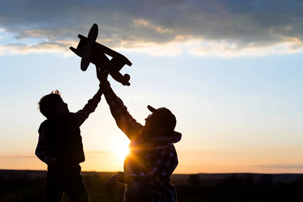 父亲和儿子在日落时分在公园里玩纸板玩具飞机 友好家庭的概念 人们在户外玩得很开心在深蓝色天空的背景上拍摄的图像 — 图库照片
