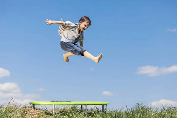 少年はその日のうちに畑で遊んでいた 屋外で楽しんでいる人 彼は芝生の上のトランポリンでジャンプする 友好的な家族の概念 — ストック写真