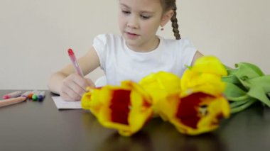 Mutlu küçük kız, annesi için masaya bir tatil kartı hazırlıyor. Mutlu Anneler Günü kavramı.