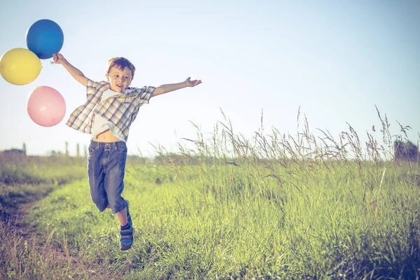 快乐的小男孩在路上玩的时候 他在田里跑着 手里拿着气球 孩子在玩大自然的把戏幸福的概念 — 图库照片