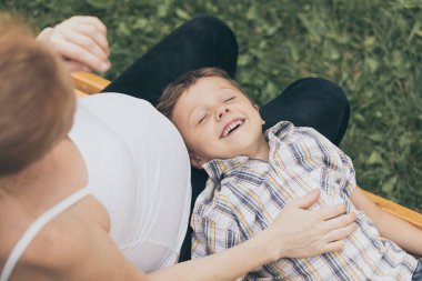 Mutlu küçük çocuk gündüz vakti parkta annesine sarılıyor. Doğada eğleniyoruz. Mutluluk kavramı.