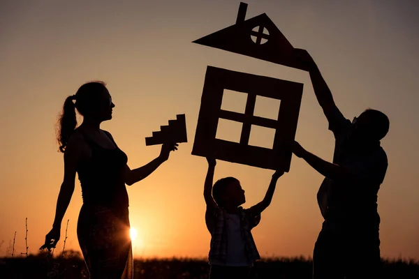 Happy family standing on the field at the sunset time. They build a house. Concept of friendly family.