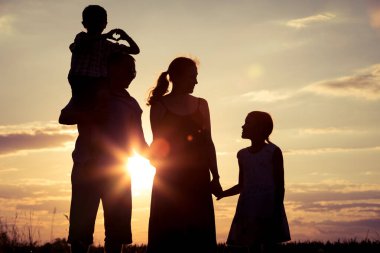Mutlu aile gün batımında parkta duruyor. İnsanlar dışarıda eğleniyor. Arkadaş canlısı aile kavramı.