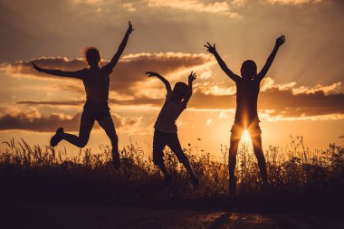 Gün batımında sahada oynayan üç mutlu çocuğun silueti. İnsanlar dışarıda eğleniyor. Arkadaş canlısı aile kavramı.