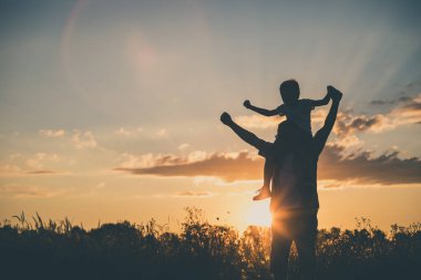 Baba ve oğul günbatımı anda parkta oynamak. İnsanlar sahada eğleniyor. Kavram dostu aile ve yaz tatili.