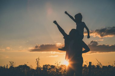 Baba ve oğul günbatımı anda parkta oynamak. İnsanlar sahada eğleniyor. Kavram dostu aile ve yaz tatili.