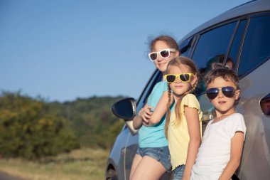 Mutlu erkek ve iki kız kardeşi o saatte arabanın yanında duruyorlar. Çocuklar dışarıda eğleniyor. Aile kavramı seyahate hazır..