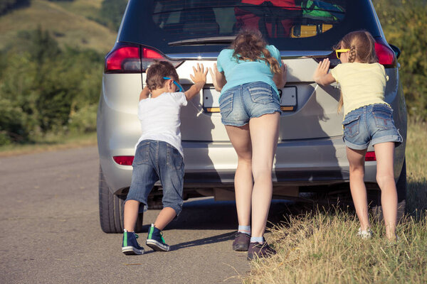 Happy brother and his two sisters are standing near the car at the day time. Children having fun outdoors. Concept of the family is ready for travel.