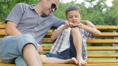 Baba ve oğul gündüz vakti parkta bankta oturuyorlar. Spinner 'la oynuyorlar. Arkadaş canlısı aile kavramı.
