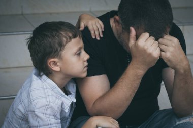 Gündüz vakti dışarıda oturan üzgün küçük bir çocuğun ve babanın portresi. Üzüntü kavramı.