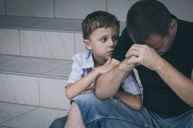 Gündüz vakti dışarıda oturan üzgün küçük bir çocuğun ve babanın portresi. Üzüntü kavramı.