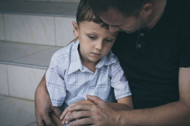 Gündüz vakti dışarıda oturan üzgün küçük bir çocuğun ve babanın portresi. Üzüntü kavramı.