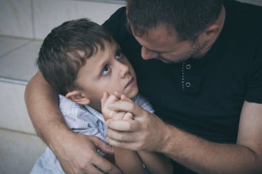 Gündüz vakti dışarıda oturan üzgün küçük bir çocuğun ve babanın portresi. Üzüntü kavramı.