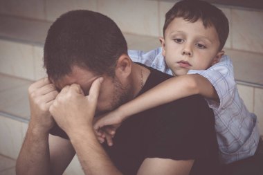 Gündüz vakti dışarıda oturan üzgün küçük bir çocuğun ve babanın portresi. Üzüntü kavramı.