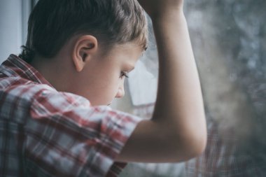 Gündüz vakti pencerenin yanında oturan üzgün küçük bir çocuğun portresi..