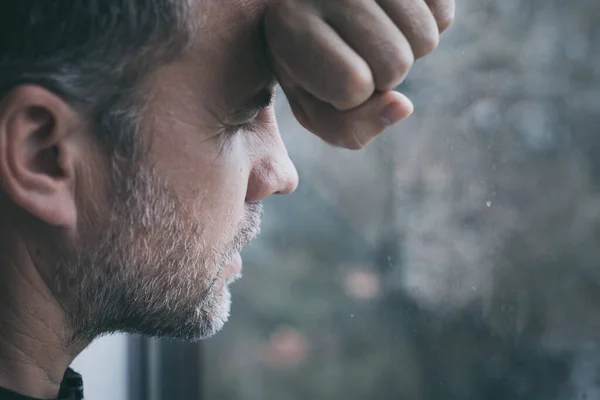 窓の近くに立って顔を覆う悲しい男の肖像画 — ストック写真