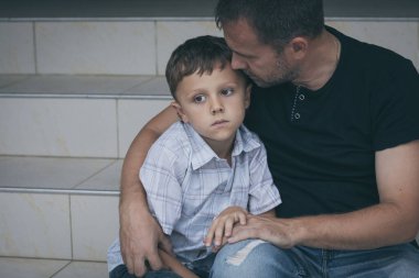 Gündüz vakti dışarıda oturan üzgün küçük bir çocuğun ve babanın portresi. Üzüntü kavramı.