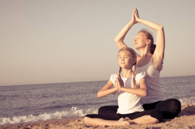 Anne ve kızı gündüz vakti plajda yoga egzersizleri yapıyor. İnsanlar dışarıda eğleniyor. Yaz tatili ve arkadaş canlısı aile kavramı.