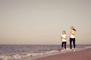 Anne ve kızı gündüz kumsalda koşuyorlar. İnsanlar dışarıda eğleniyor. Yaz tatili ve arkadaş canlısı aile kavramı.