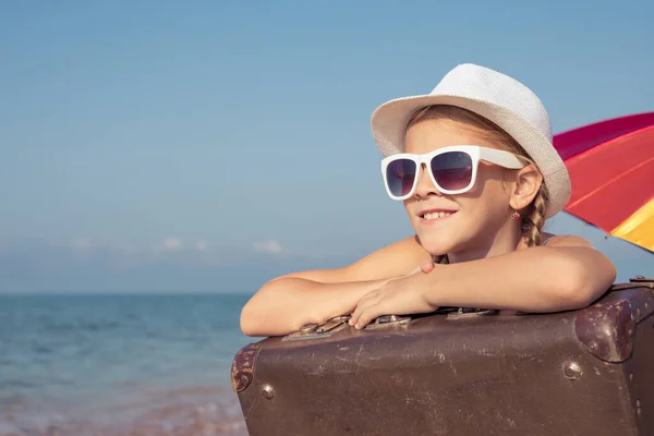ビーチに座ってスーツケースを着た幸せな女の子が一人います 子供は屋外で楽しんでいる 夏休みの概念 — ストック写真
