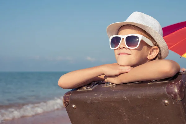 ビーチに座ってスーツケースを着た幸せな女の子が一人います 子供は屋外で楽しんでいる 夏休みの概念 — ストック写真