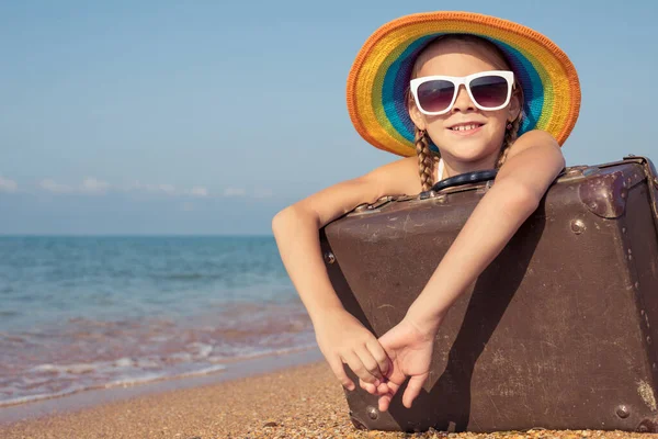 ビーチに座ってスーツケースを着た幸せな女の子が一人います 子供は屋外で楽しんでいる 夏休みの概念 ストック写真