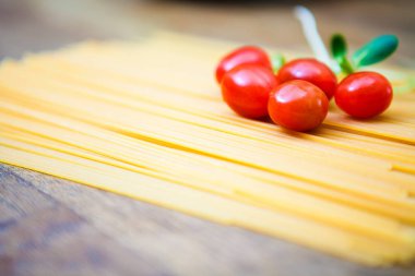 Pişmemiş spagetti ve bir tahta üzerinde domates 