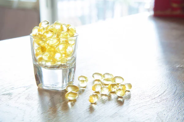 Fish oil, soft capsule, omega, supplement in glass on wooden tab