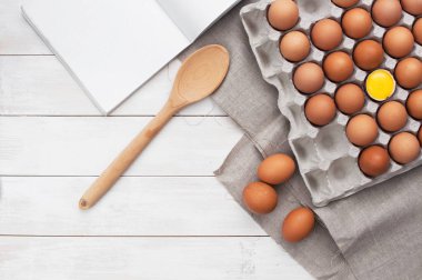 Beyaz ahşap tablo kopya alanı ile tavuk yumurtası, mutfak defter ve kaşık Üstten Görünüm.