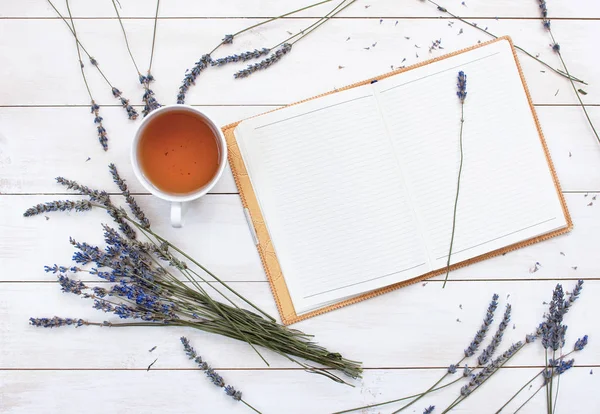 Bir fincan çay, lavanta ve bir defter üstten görünüm Beyaz ahşap zemin üzerinde.
