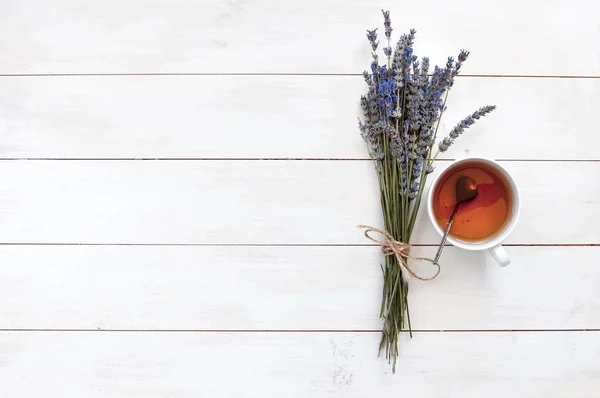 A cup of hot tea and lavender on a white wooden background top view.