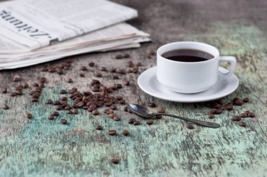 Dağınık tahıl ve gazete ile ahşap bir masa üzerinde siyah kahve bir fincan. Siyah kahve sıcak içecek tahıl gazete ahşap arka plan beyaz fincan Kahvaltı