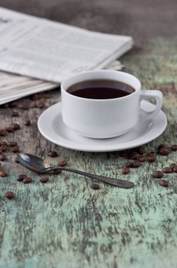 Dağınık tahıl ve gazete ile ahşap bir masa üzerinde siyah kahve bir fincan. Siyah kahve sıcak içecek tahıl gazete ahşap arka plan beyaz fincan Kahvaltı