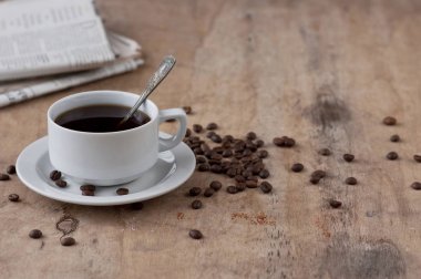 Dağınık tahıl ve gazete ile ahşap bir masa üzerinde siyah kahve bir fincan. Siyah kahve sıcak içecek tahıl gazete ahşap arka plan beyaz fincan Kahvaltı