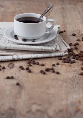 Dağınık tahıl ve gazete ile ahşap bir masa üzerinde siyah kahve bir fincan. Siyah kahve sıcak içecek tahıl gazete ahşap arka plan beyaz fincan Kahvaltı
