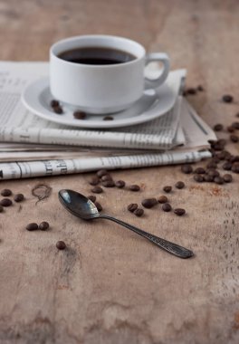 Dağınık tahıl ve gazete ile ahşap bir masa üzerinde siyah kahve bir fincan. Siyah kahve sıcak içecek tahıl gazete ahşap arka plan beyaz fincan Kahvaltı