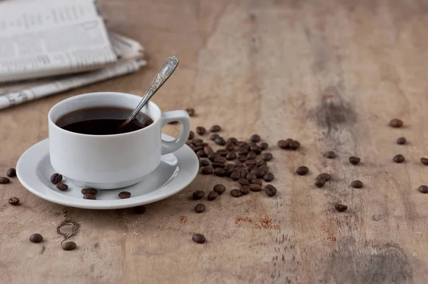 Dağınık tahıl ve gazete ile ahşap bir masa üzerinde siyah kahve bir fincan. Siyah kahve sıcak içecek tahıl gazete ahşap arka plan beyaz fincan Kahvaltı